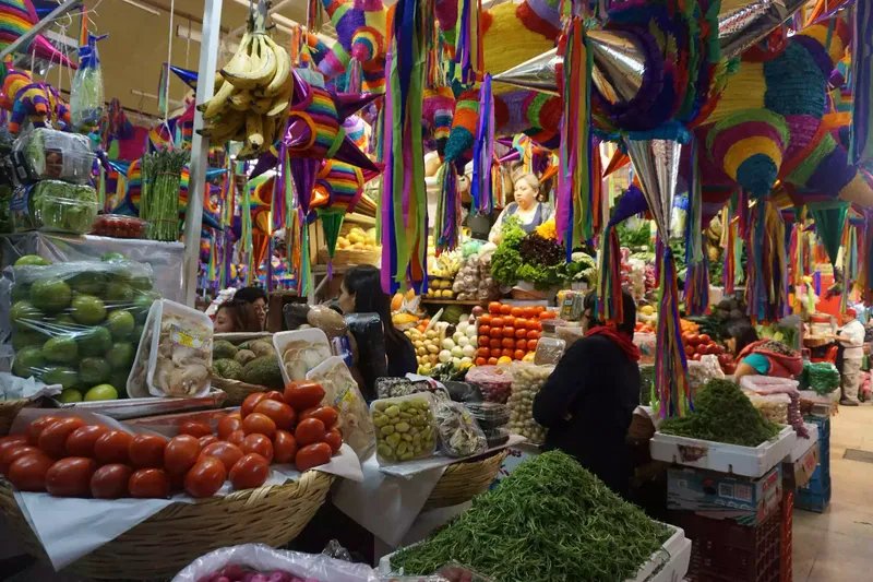 Pilas de productos frescos en un mercado con coloridas piñatas encima