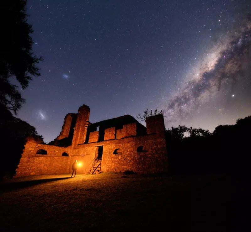 Persona con una luz de pie en las ruinas de un edificio de piedra con un cielo estrellado colgando